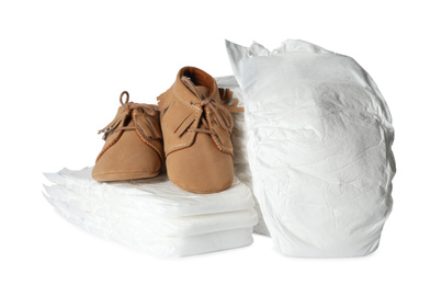 Disposable diapers and child's shoes on white background