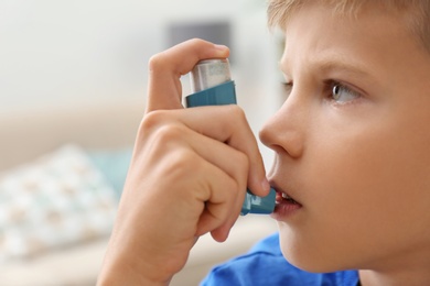 Little boy using asthma inhaler on blurred background