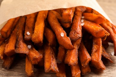 Paper bag with tasty sweet potato fries on table, closeup