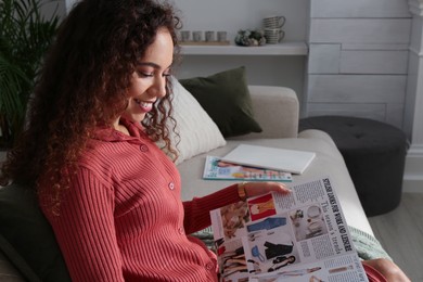 Young African-American woman reading fashion magazine at home