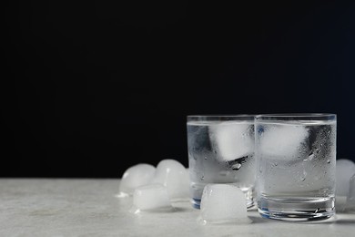 Shot glasses of vodka with ice on light grey table against black background. Space for text
