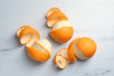 Photo of Peeled fresh oranges with zest preparing for drying on white marble table, flat lay