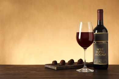 Bottle and glass of red wine with chocolate candies on wooden table. Space for text