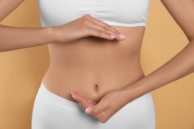 Photo of Woman in underwear holding something near her belly on beige background, closeup. Healthy stomach