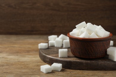 Bowl and white sugar cubes on wooden table. Space for text