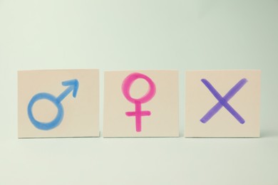 Photo of Gender identity concept. Cards with cross mark and gender symbols on light background