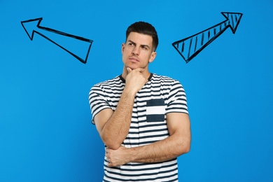 Pensive man standing near blue wall with arrows