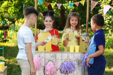Cute little girls selling natural lemonade to boys in park. Summer refreshing drink