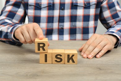 Man making word Risk of cubes at wooden table, closeup