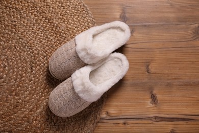 Photo of Pair of warm stylish slippers and wicker mat on wooden floor, flat lay