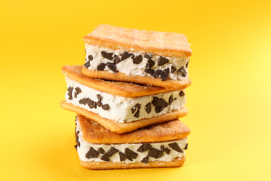 Sweet delicious ice cream cookie sandwiches on yellow background, closeup