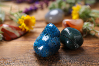 Different gemstones and healing herbs on wooden table, closeup