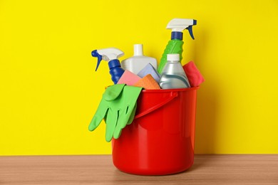 Bucket with different cleaning supplies on wooden floor near yellow wall