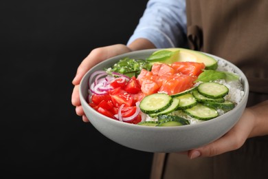 Woman holding delicious poke bowl with salmon and vegetables on black background, closeup