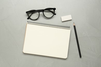Sketchbook, glasses, pencil and eraser on light grey table, flat lay