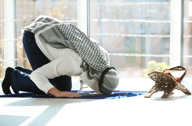 Muslim man with Koran praying on rug indoors