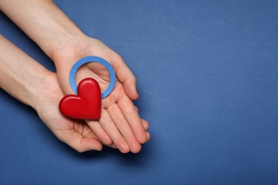 Woman showing blue paper circle as World Diabetes Day symbol and red heart on color background, top view with space for text