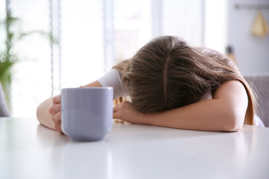 Young woman with cup of drink sleeping at home in morning