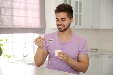 Happy young man with tasty yogurt at table in kitchen