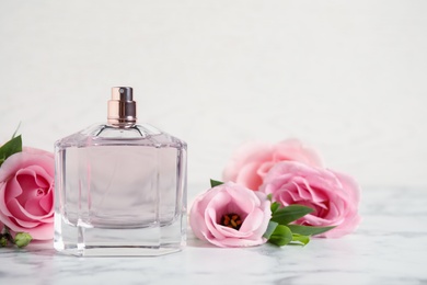 Bottle of perfume and beautiful flowers on white marble table. Space for text