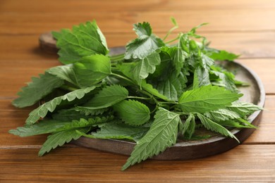 Photo of Board with fresh stinging nettle leaves on wooden table, closeup