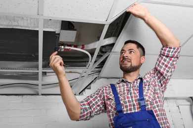 Professional technician repairing ceiling mounted air conditioner indoors