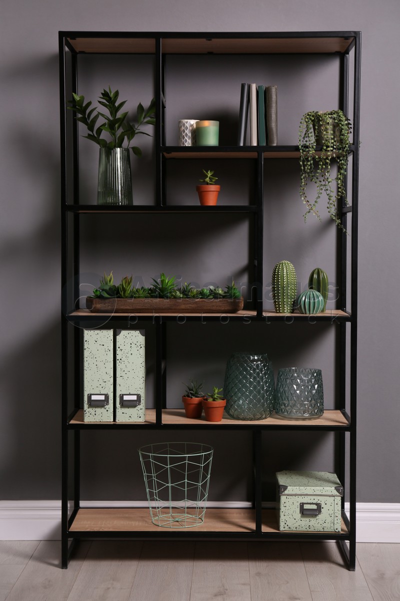 Photo of Shelving with different decor, books and houseplants near gray wall. Interior design