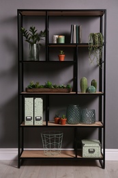 Shelving with different decor, books and houseplants near gray wall. Interior design