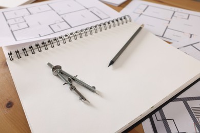 Sketchbook with construction drawings, pair of compasses and pencil on wooden table, closeup