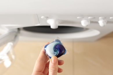 Woman holding laundry detergent capsule near washing machine indoors, top view