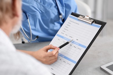 Doctor showing medical card to patient at table in clinic, closeup