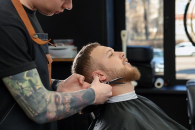 Professional hairdresser working with bearded client in barbershop