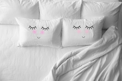 Soft pillows with cute faces on comfortable bed, above view