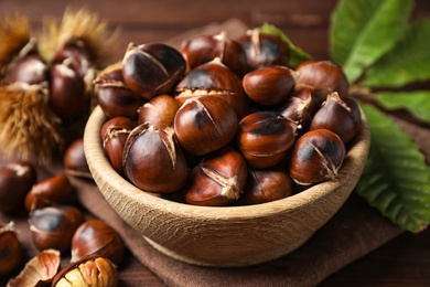 Delicious roasted edible chestnuts in wooden bowl on table, closeup