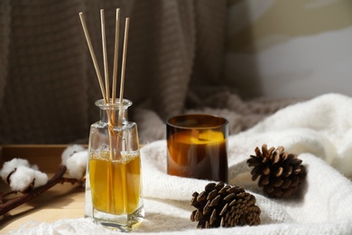 Photo of Reed air freshener, candle and pine cones on wooden tray indoors