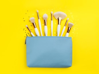 Different makeup brushes, case and shiny confetti on yellow background, flat lay