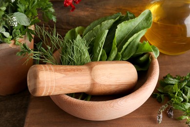 Photo of Mortar with pestle, fresh green herbs and oil on wooden table