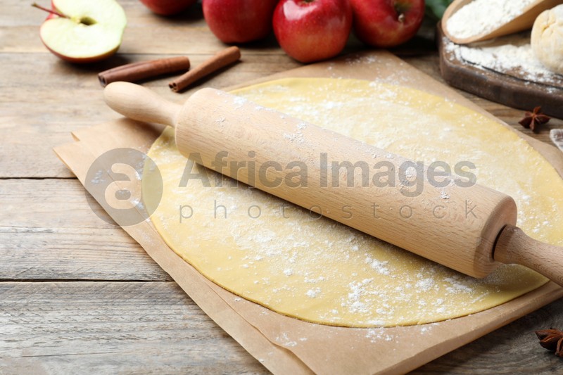 Rolling pin, raw dough and ingredients on wooden table, closeup. Baking apple pie