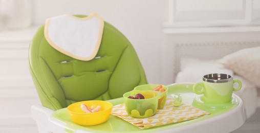 High chair with food in baby tableware on tray indoors. Banner design