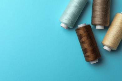 Different colorful sewing threads on light blue background, flat lay. Space for text