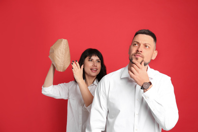 Woman popping paper bag behind her friend's back on red background. April fool's day
