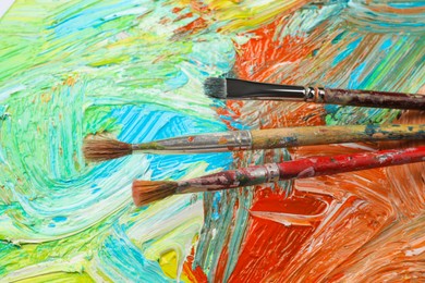 Closeup view of artist's palette with mixed paints and brushes as background