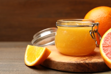 Delicious orange marmalade in jar and fresh fruits on wooden table, closeup. Space for text