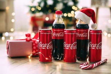 MYKOLAIV, UKRAINE - January 01, 2021: Bottles and cans of Coca-Cola on floor against blurred Christmas lights