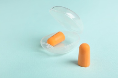 Pair of orange ear plugs and case on turquoise background