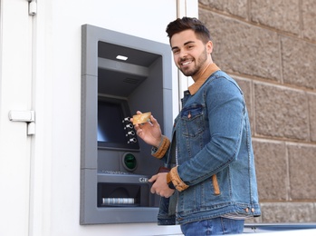 Photo of Young man with credit card near modern cash machine outdoors