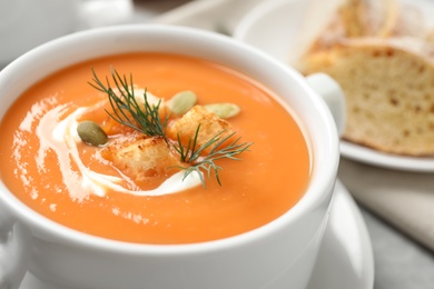 Tasty creamy pumpkin soup with croutons, seeds and dill in bowl on table, closeup