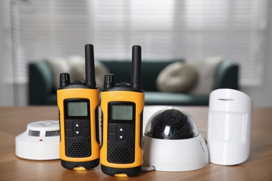 CCTV camera, walkie talkies, smoke and movement detectors on wooden table indoors. Home security system