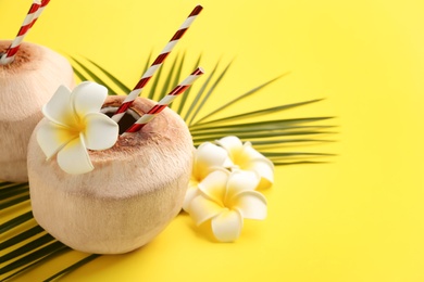 Fresh coconuts with drinking straws and flowers on yellow background. Space for text