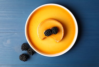 Photo of Delicious pudding with caramel and blackberries on blue wooden table, flat lay